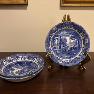 May include: Two blue and white porcelain bowls with a landscape design. One bowl is displayed on a gold-colored stand. The other two bowls are stacked. The bowls have a scalloped edge.