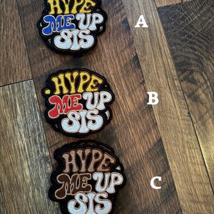 May include: Three embroidered patches with the text "HYPE ME UP SIS". The patches are in different color schemes: yellow and blue, yellow and red, and brown and tan. Each patch has a black border.