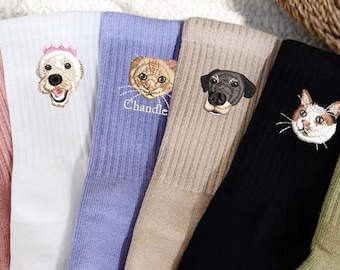 May include: A collection of colorful, ribbed socks, each embroidered with a different pet's face. The socks are in shades of pink, white, lavender, tan, black, and olive green. Some socks have pet names embroidered below the pet's face.