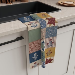 Könnte beinhalten: Ein Patchwork-Küchentuch mit verschiedenen Blumen- und Sternmustern in Blau-, Rot-, Grün- und Gelbtönen. Das Tuch hängt über einem Küchenbecken und zeigt sein dekoratives Design und seinen Landhausstil.