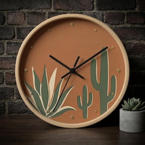 May include: Round wall clock with a light wood frame and a terracotta-colored face. The clock features a desert-themed design with green cacti and agave plants. Black clock hands and gold-colored markers complete the design.