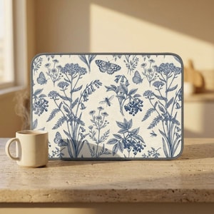 May include: A rectangular kitchen mat with a blue and white floral and butterfly pattern. The mat displays detailed illustrations of plants, insects, and butterflies. A beige mug sits on a stone countertop next to the mat.