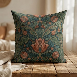 Könnte beinhalten: Quadratisches Zierkissen mit einem detaillierten Blumenmuster in Grün-, Blau- und Orangetönen. Das Design zeigt stilisierte Blumen und Blätter und erzeugt eine Vintage-Ästhetik. Das Kissen liegt auf einer Holzoberfläche.
