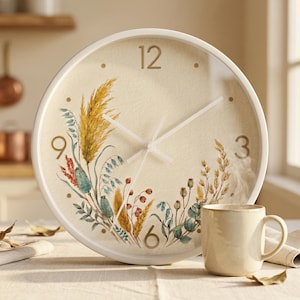 May include: A cream-coloured wall clock with a white frame. The clock face has a floral design with wheat and botanical elements. A beige mug is positioned to the right of the clock.