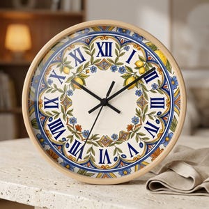 May include: A round wall clock with a light wood frame featuring a cream-colored face decorated with a blue, yellow, and green botanical pattern of lemons and flowers. The clock has black hands and dark blue Roman numerals for the hour markers.