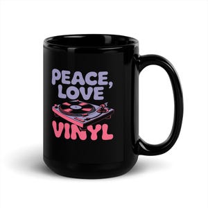May include: Black ceramic mug with the words "PEACE, LOVE, VINYL" in lavender and pink. A pink and purple turntable graphic is centered below the words. The mug has a large handle and is suitable for hot or cold beverages.