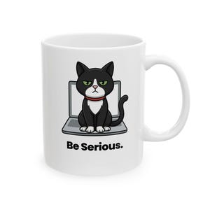 Peut inclure: Mug en céramique blanche avec un chat noir et blanc de dessin animé portant un collier rouge, assis sur un ordinateur portable. Le texte "Be Serious." est imprimé en noir sous l'image du chat.
