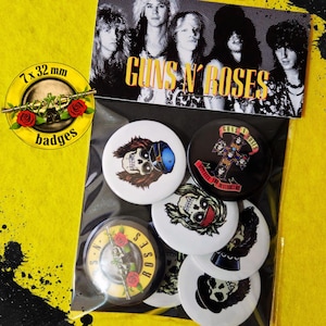 Pode incluir: Um conjunto de sete botões redondos de 32 mm com imagens dos Guns N' Roses. A coleção inclui designs com ilustrações de caveiras, o logótipo da banda e motivos de cruz em preto, branco e amarelo. Os botões estão embalados num saco de plástico transparente com um cartão de cabeçalho que mostra os membros da banda e o texto Guns N' Roses.