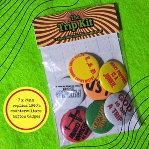 May include: A set of seven 25mm round button badges in a clear plastic package with a header card titled The Trip Kit. The badges feature various colours including yellow, orange, green, white, and red with printed text and graphic designs.