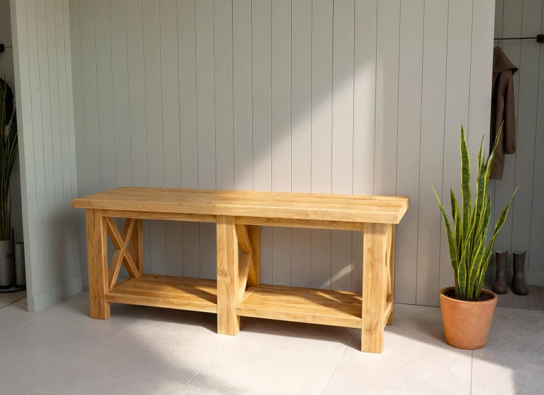 DIY Farmhouse X-Base Bench made of light-toned rustic wood featuring a 54-inch length, 17.5-inch depth, and 19.5-inch height. The bench has a thick timber top, decorative X-frame legs, and a lower storage shelf, pictured outdoors on a stone patio.