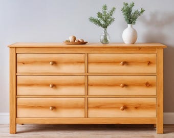 May include: A light-colored wooden dresser with six drawers and round wooden knobs. The dresser is topped with a small wooden tray holding several round objects. Two vases with greenery are on top.