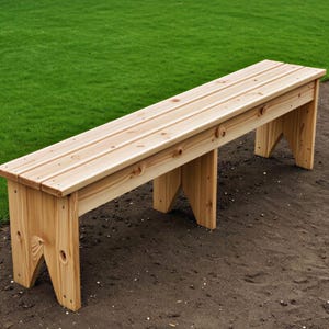 May include: A natural wood bench with a slatted seat and angled legs. The bench is made of light-colored wood and is set on a bed of dirt with a green grassy background. A simple outdoor seating option.