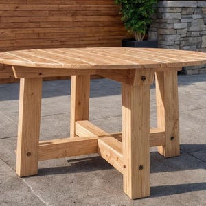 May include: A round wooden table with a light brown finish. The table has a slatted top and four sturdy, square legs. The legs are connected by a cross-beam for added stability. The table is suitable for outdoor use.