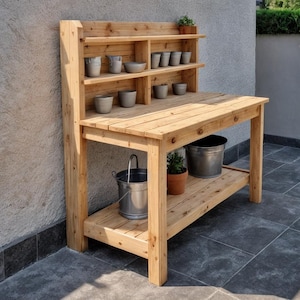 May include: A wooden potting bench with a natural finish. It features a tabletop, a lower shelf, and an upper shelf with multiple compartments. Several gray pots and metal buckets are visible, suggesting a gardening theme.