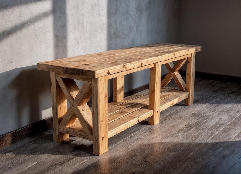 DIY Farmhouse X-Base Bench made of light-toned rustic wood featuring a 54-inch length, 17.5-inch depth, and 19.5-inch height. The bench has a thick timber top, decorative X-frame legs, and a lower storage shelf, pictured outdoors on a stone patio."