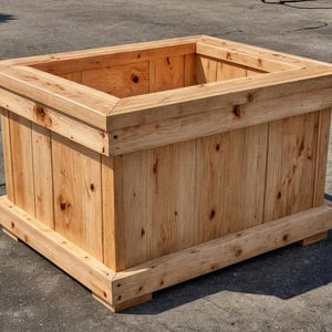 Puede incluir: Una jardinera rectangular grande de madera. La caja está construida con tablas de madera de color claro, con una abertura cuadrada en la parte superior. El diseño presenta un borde superior decorativo y una base, creando una apariencia robusta y rústica. Ideal para jardinería al aire libre.