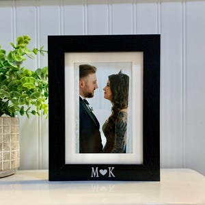 May include: Black picture frame with a white mat and a photo of a couple looking at each other. The frame has the initials "M" and "K" with a heart in between.