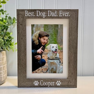 May include: A rustic wood picture frame with a white mat and a photo of a man and a dog. The frame has the text "Best. Dog. Dad. Ever." and "Cooper" with paw prints on the bottom.