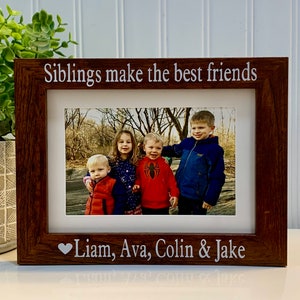 May include: A rectangular dark wood picture frame with white text engraved on the border. The top border reads Siblings make the best friends and the bottom border features a heart icon followed by the names Liam, Ava, Colin & Jake.