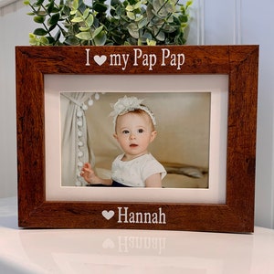 May include: A brown wooden picture frame with a white mat. The frame has the text "I ♥ my Pap Pap" at the top and "♥ Hannah" at the bottom. The frame contains a photo of a young girl with a white headband and a white dress.