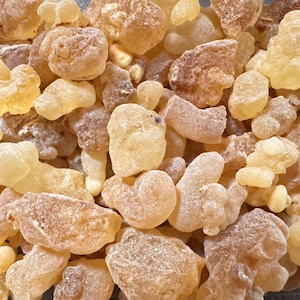Puede incluir: Una colección de trozos de resina de incienso cruda de diversos tamaños y formas. Los trozos de resina muestran un aspecto de translúcido a opaco con una paleta de colores que va desde el crema pálido y amarillo claro hasta el ámbar cálido y tonos parduzcos.