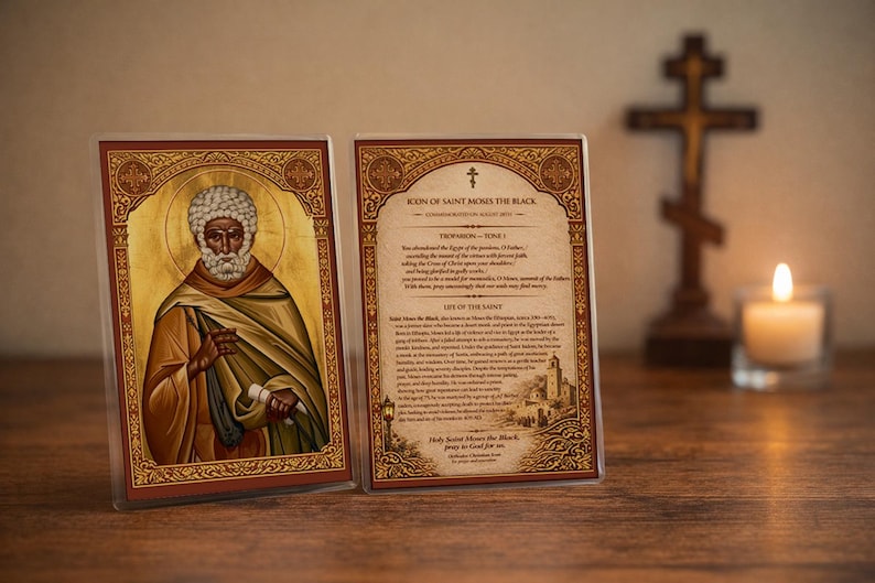 Puede incluir: Dos iconos enmarcados de San Mois&eacute;s el Negro, con detalles dorados e ilustraciones detalladas. El texto en el icono de la derecha describe la vida del santo. Una cruz de madera y una vela encendida est&aacute;n en el fondo, creando un ambiente espiritual.