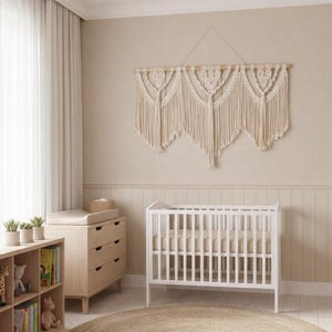Könnte beinhalten: Ein neutrales Kinderzimmer mit einem weißen Kinderbett, einer Holzkommode und einem runden Jute-Teppich. Über dem Kinderbett hängt ein Wandbehang aus cremefarbenem Makramee. Der Raum ist von natürlichem Licht durchflutet.