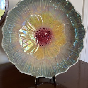 Peut inclure: Un bol rond en céramique présentant un motif de fleur sculpté avec un bord festonné. Le bol possède une finition irisée avec un centre jaune, des étamines rouge foncé et des pétales bleu clair qui scintillent d'un éclat nacré sur la surface.