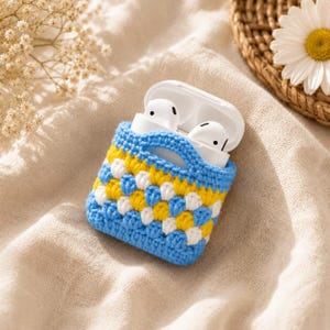 May include: A white wireless earbud charging case encased in a handmade crochet cover featuring a checkered pattern of bright yellow, white, and light blue yarn. The protective sleeve has a snug fit with a cutout for the lid to open easily.