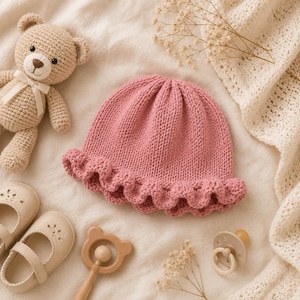 Puede incluir: Un gorro de bebé tejido en color rosa empolvado con borde de volantes, acompañado de un oso de peluche de ganchillo beige con cinta blanca, un par de zapatos beige con recortes florales, un sonajero de madera con forma de oso y un chupete de silicona beige.