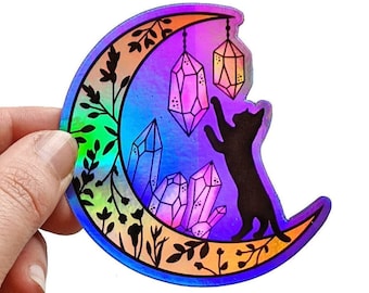May include: Holographic sticker of a crescent moon with a black cat reaching for crystals hanging from it. The moon is surrounded by floral designs and the background is a rainbow gradient.