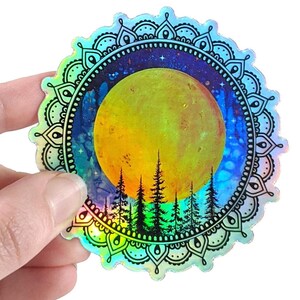 May include: Holographic sticker featuring a yellow moon, silhouetted trees, and a starry night sky. The design is framed by a black and white mandala pattern. The sticker has a rainbow iridescent effect.
