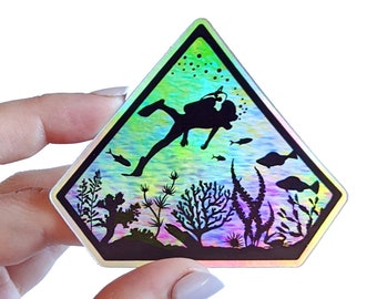 May include: A holographic sticker featuring a diver silhouette in a diamond-shaped warning sign. The diver is surrounded by underwater plants and fish. The sticker has a rainbow iridescent finish.