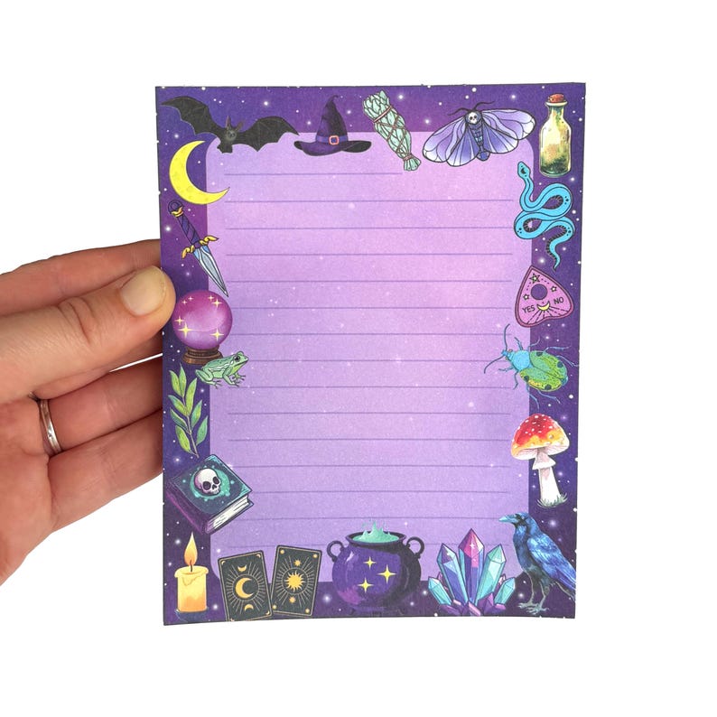 May include: A purple lined notepad with a border of witchy illustrations. The illustrations include a bat, witch hat, sage bundle, moth, bottle, snake, planchette, beetle, mushroom, raven, crystals, cauldron, tarot cards, and a candle.