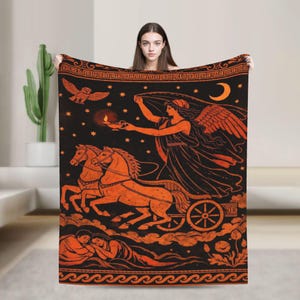 May include: Black blanket with an orange illustration of a woman in a chariot pulled by two horses. The design includes an owl, stars, a crescent moon, and a decorative border. The blanket is held up by a person.