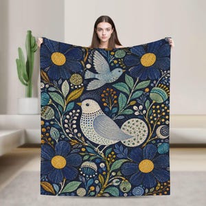 May include: A rectangular throw blanket featuring a dark blue background with a repeating pattern of large blue flowers with yellow centers, green leaves, and two birds. One bird is perched while the other is depicted in flight above it.