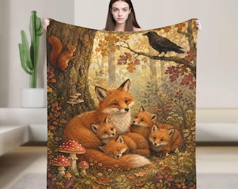 May include: A rectangular throw blanket featuring a detailed forest scene with a mother fox and three kits resting on the ground. A squirrel is perched on a tree trunk to the left, and a black crow sits on a branch above. The scene includes mushrooms.