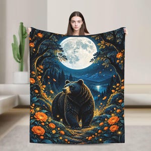 May include: A rectangular throw blanket featuring a dark forest scene at night with a large full moon, a black bear standing in the foreground, and vibrant orange flowers scattered throughout the landscape under a starry sky.