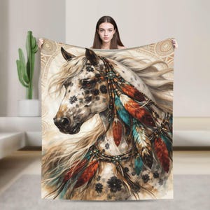 May include: A rectangular throw blanket featuring a detailed illustration of a spotted horse with a flowing mane. The horse is adorned with decorative beaded headgear and colorful feathers in shades of red, orange, and teal against a cream background.