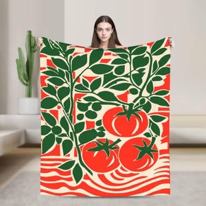 May include: A blanket featuring a vibrant tomato plant design. The blanket showcases a repeating pattern of red tomatoes, green leaves, and stems against a cream and red background. The blanket is a cozy home decor item.