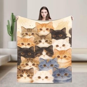 May include: A rectangular throw blanket featuring a repeating pattern of various cat faces in shades of orange, brown, black, white, and gray. The cats have large, expressive eyes and fluffy fur, arranged in a dense, overlapping collage design.