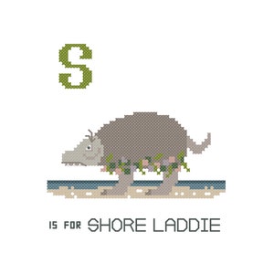 May include: A green letter S with a grey, cartoon shore creature wearing a floral crown. The creature is standing on a beach with blue water. The text 'S is for Shore Laddie' is below the creature.