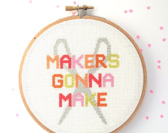 May include: A white embroidery hoop with a cross-stitch design that reads "Makers Gonna Make" in colorful letters. The design also includes a pair of scissors.