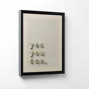 May include: A framed artwork with the words "yes you can" in a 3D font. The text is in a light green color and is placed on a beige background. The frame is black.