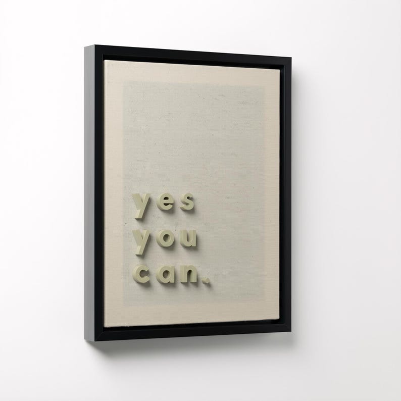 May include: A framed artwork with the words "yes you can" in a 3D font. The text is in a light green color and is placed on a beige background. The frame is black.