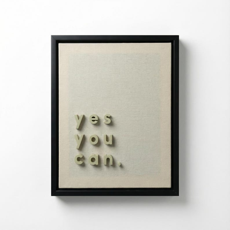May include: Framed artwork with the words "yes you can" in 3D lettering. The text is in a light green color and is placed on a beige canvas. The frame is black and the background is white.