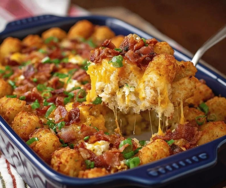 Pode incluir: Uma ca&ccedil;arola assada em um prato azul, com tater tots dourados, queijo cheddar derretido, bacon esfarelado e cebolinha picada. Uma por&ccedil;&atilde;o &eacute; levantada com um utens&iacute;lio para servir, mostrando as camadas de queijo e saborosas.
