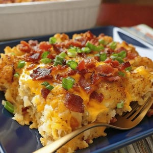 Pode incluir: Uma por&ccedil;&atilde;o de ca&ccedil;arola dourada, coberta com queijo derretido, peda&ccedil;os de bacon e cebolinhas picadas. Um garfo dourado repousa sobre um prato quadrado azul, pronto para servir.
