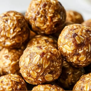 May include: Close-up of several round, brown energy bites. The bites are made with oats and other ingredients, creating a textured appearance. The image is well-lit, highlighting the details of the food.