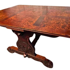 May include: A rectangular wooden table with a dark brown finish. The tabletop has a patterned design, and the table is supported by a decorative base. The table measures approximately 48 inches long and 36 inches wide.